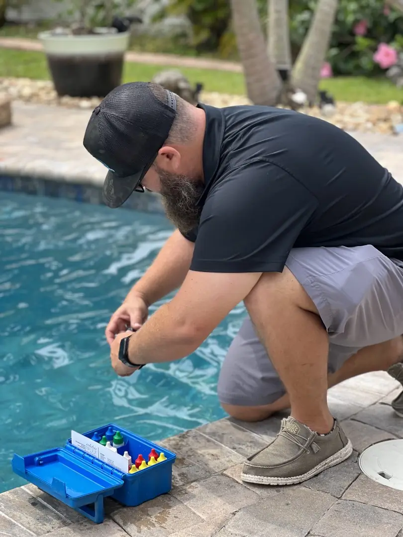 Dennis, the owner and instructor, kneeling at a pool edge reading a drop-test kit over the water