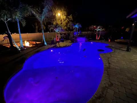 Night view of a pool glowing blue beside a paver patio
