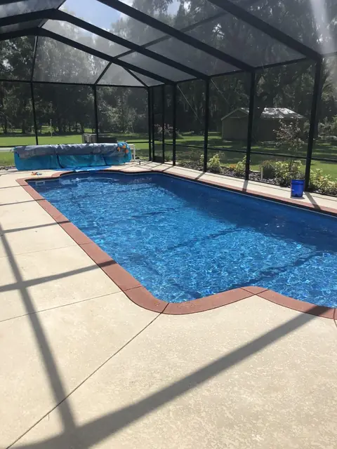 Rectangular pool with a brick-edged paver deck under a screen
