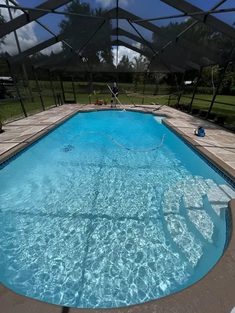 Screened-in pool with clear blue water and a paver deck