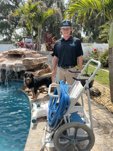 A uniformed technician beside a pressure-washer and hose cart at the edge of a rock-waterfall pool